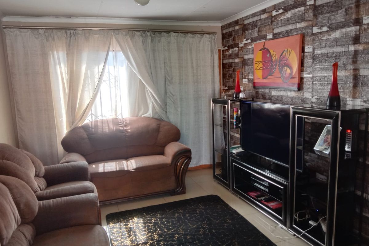 A living room featuring a textured brick-effect feature wall, tiled flooring, and large window with curtain treatments.