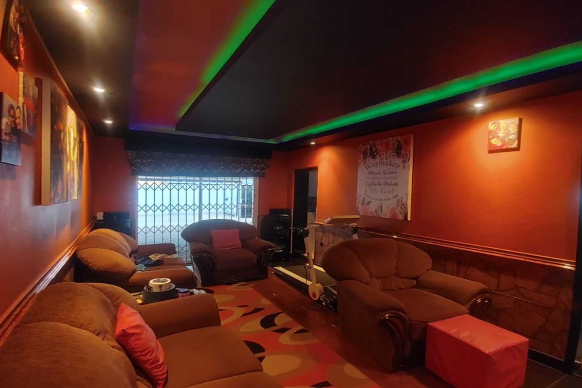 A living room featuring a recessed ceiling with integrated LED lighting, tiled flooring, and a sliding glass door with security gate.