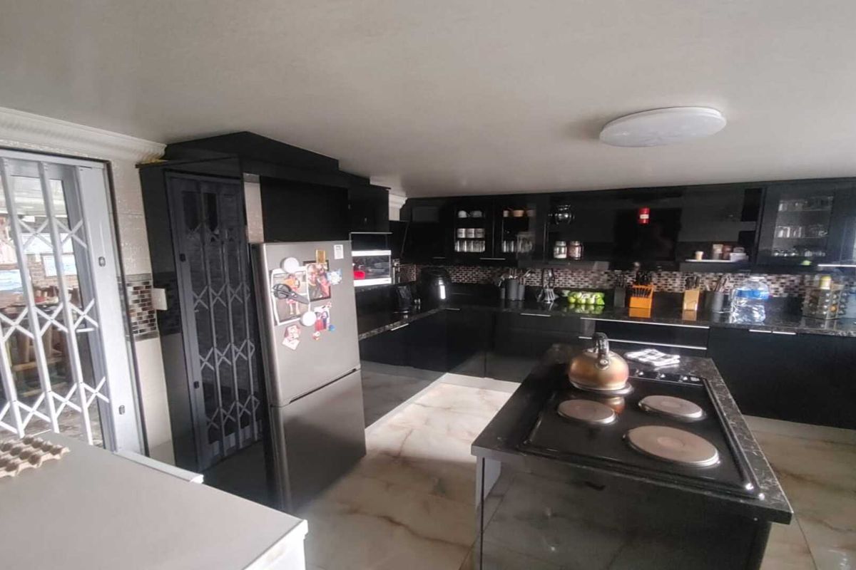 Modern kitchen featuring high-gloss black cabinetry, granite countertops, a central island with a built-in hob, and tiled flooring.