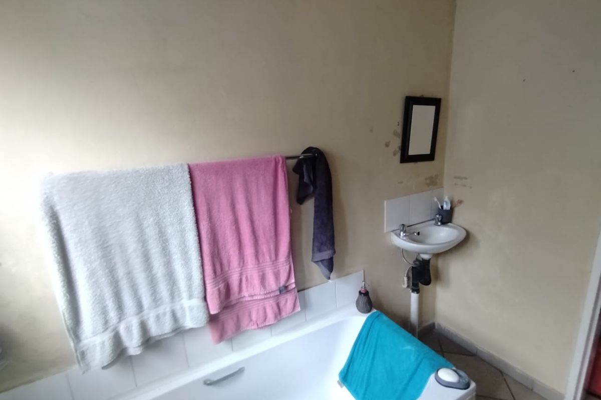 A functional bathroom featuring a built-in bathtub and a wall-mounted basin, requiring cosmetic updates to the wall finishes.
