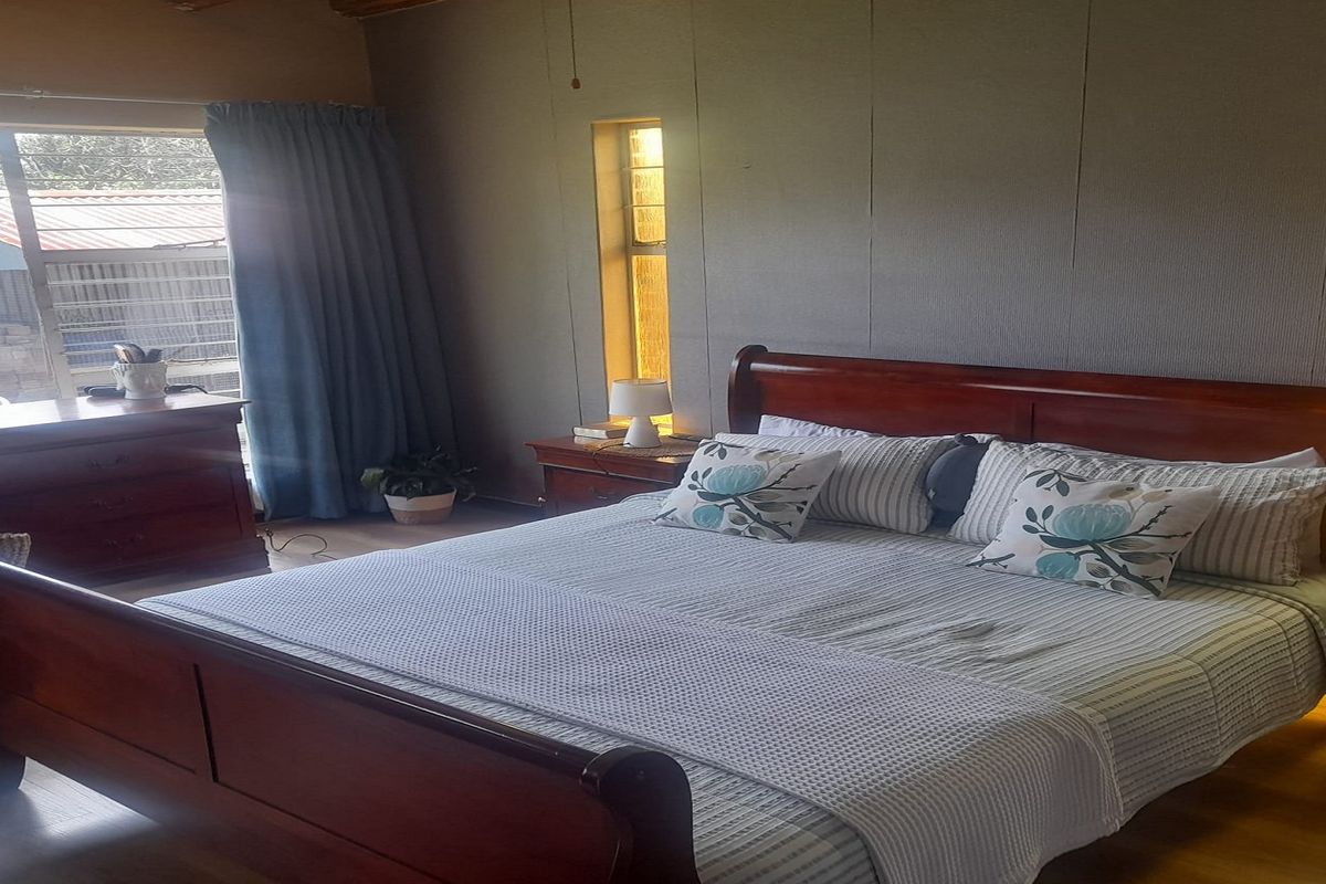 A bedroom featuring wood-look flooring, a large window with curtains, and panelled walls.