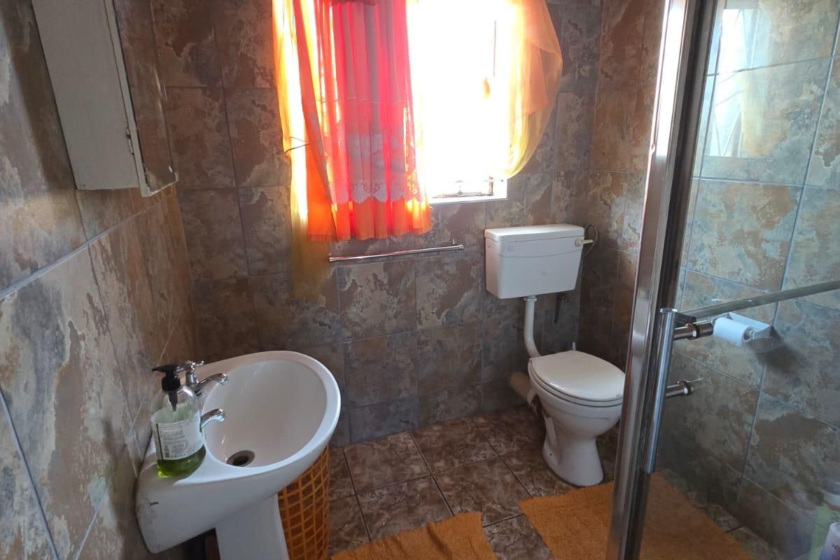 A functional bathroom featuring a pedestal basin, a standard toilet, and a glass-enclosed shower with full-height wall tiling.