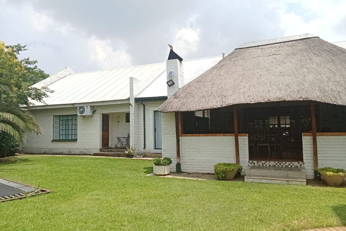 Rear view of the property featuring a white brick facade, metal roof, and a covered thatched patio area overlooking a well-maintained lawn.