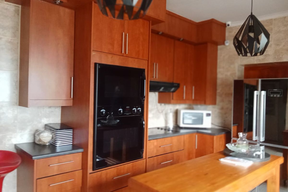 A functional kitchen featuring warm-toned wooden cabinetry, integrated oven, extractor fan, and a central wooden island bench.