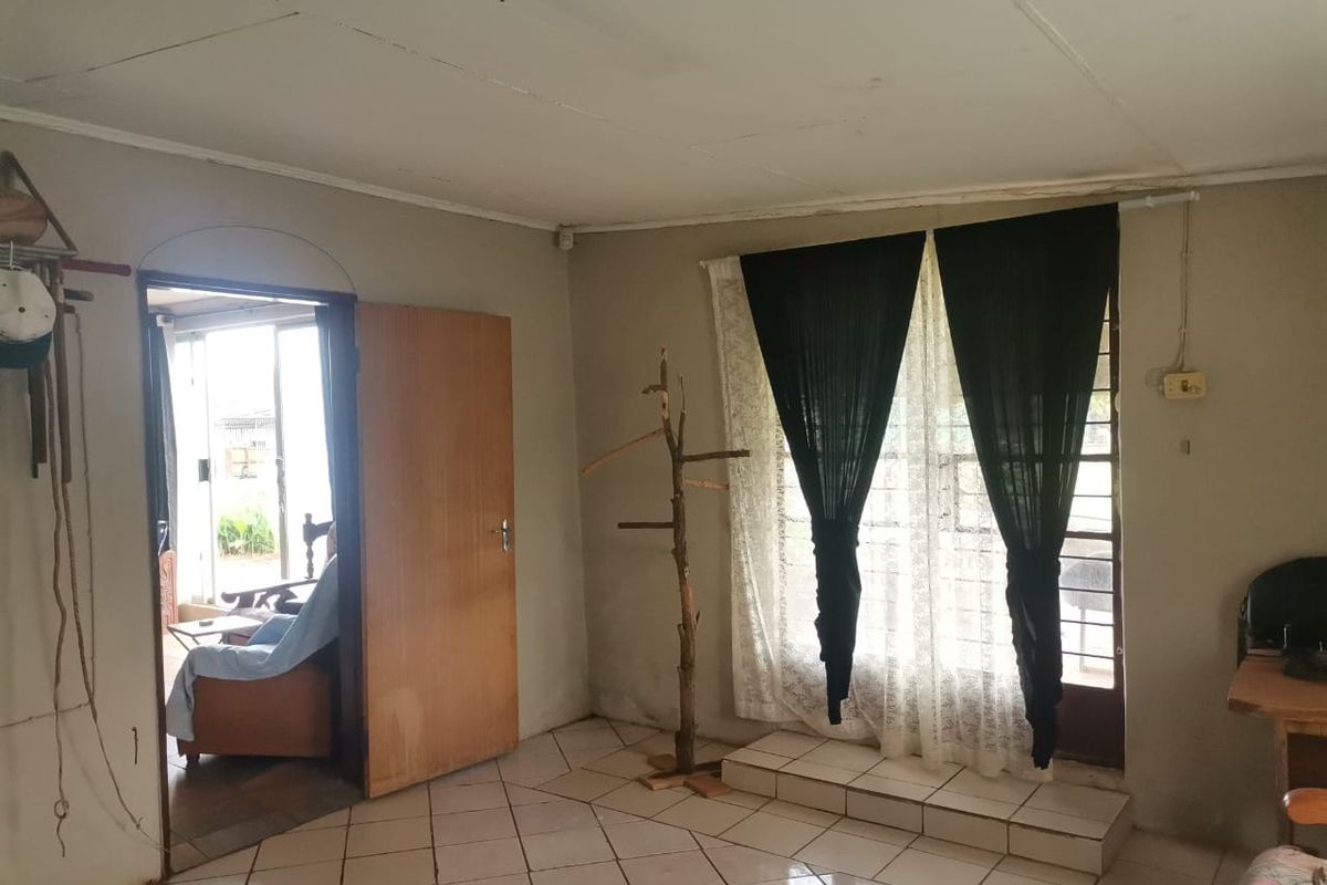 A living room area featuring tiled flooring, a doorway leading to an adjacent space, and a window with security bars.