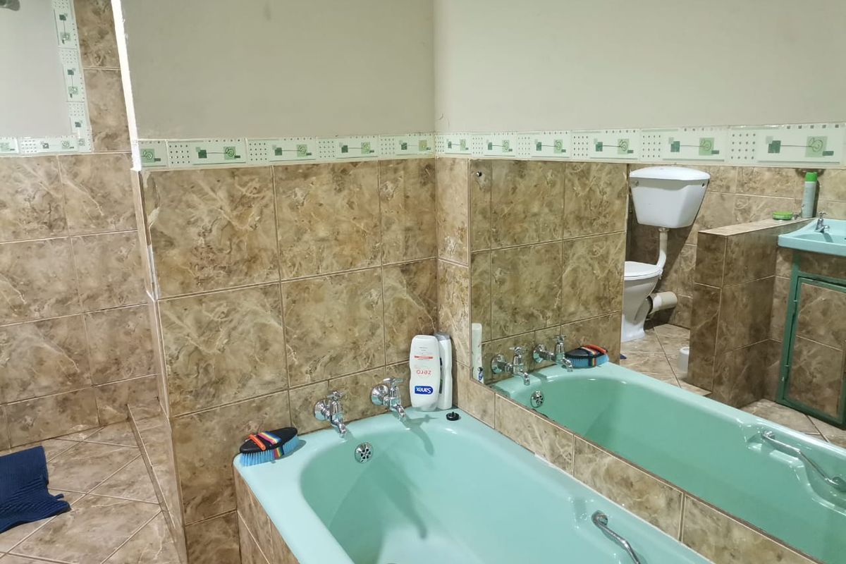 A dated bathroom featuring a vintage mint green bathtub, matching vanity, and brown marble-effect wall tiles with decorative border accents.