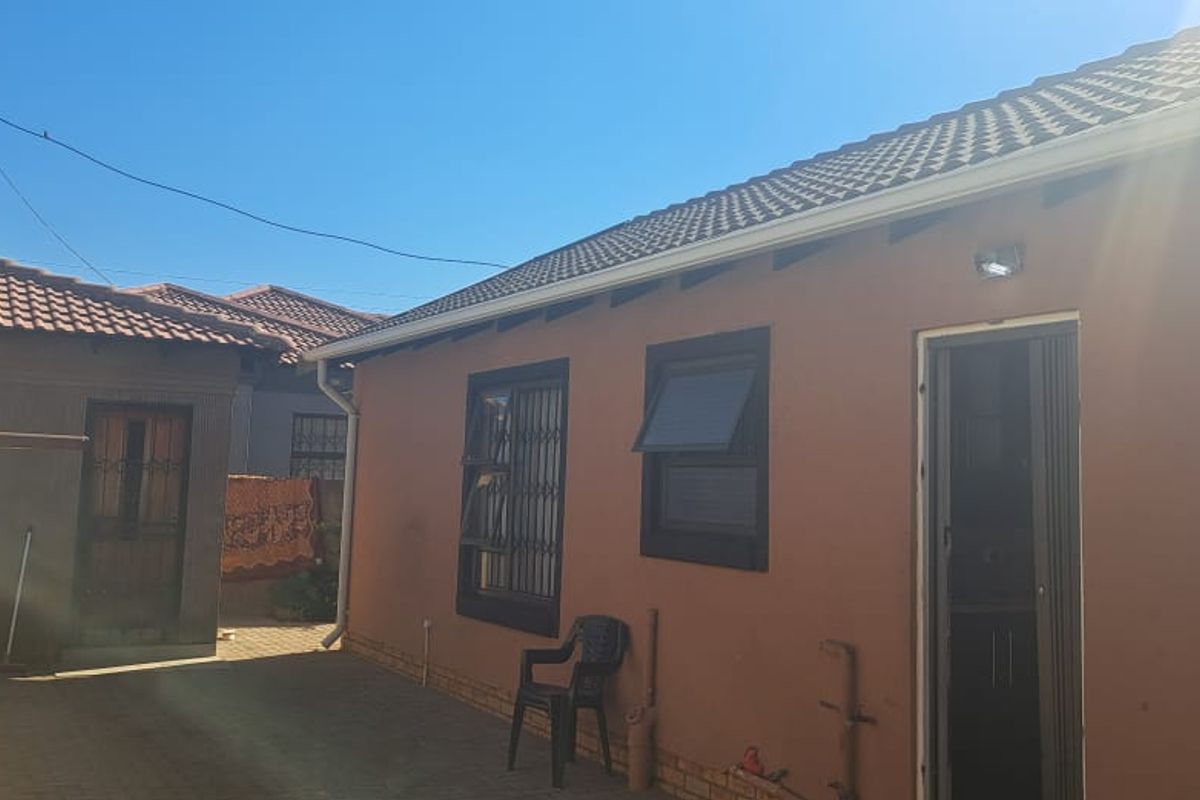 Rear exterior view of the property featuring paved courtyard area, tiled roof, and security-fitted windows and doors.