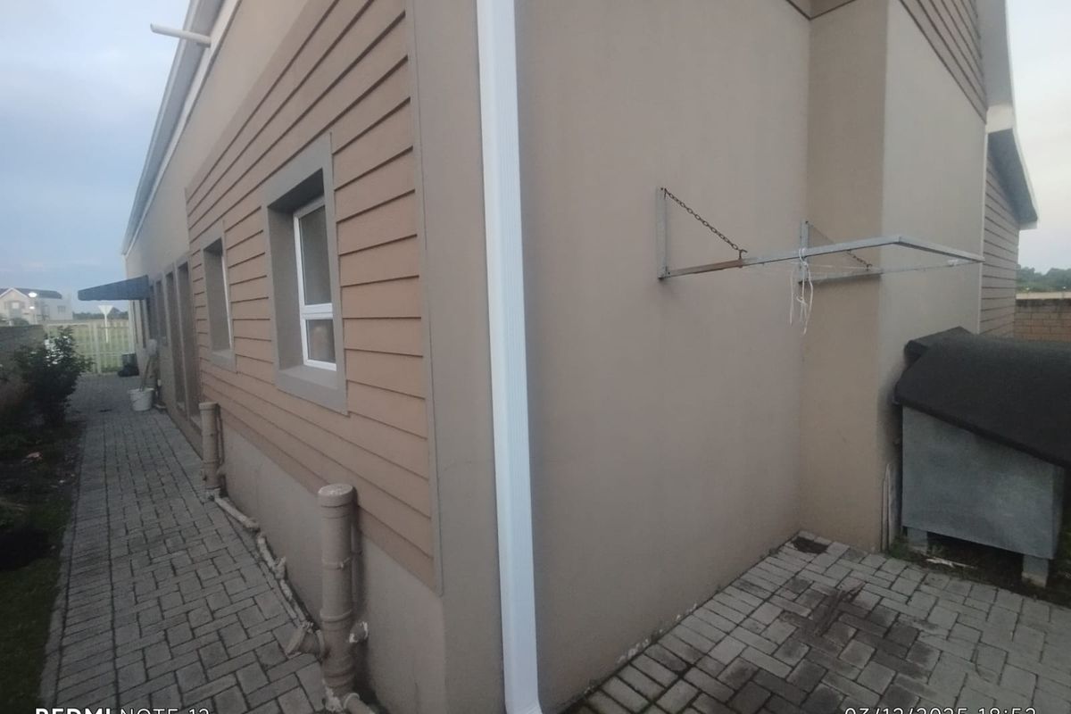 Side exterior view of the townhouse featuring paved walkway, exterior wall cladding, downpipes, and a wall-mounted drying rack.