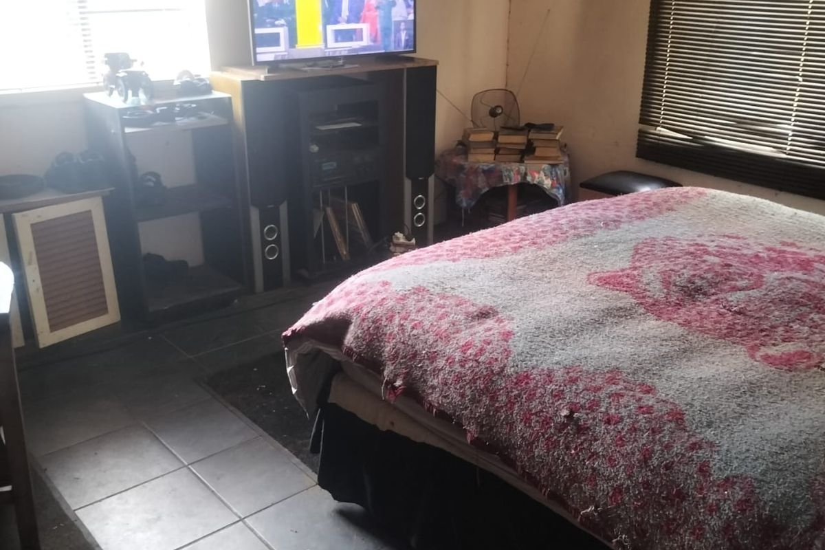A bedroom featuring tiled flooring and window blinds, currently used as a living space with built-in window fixtures.