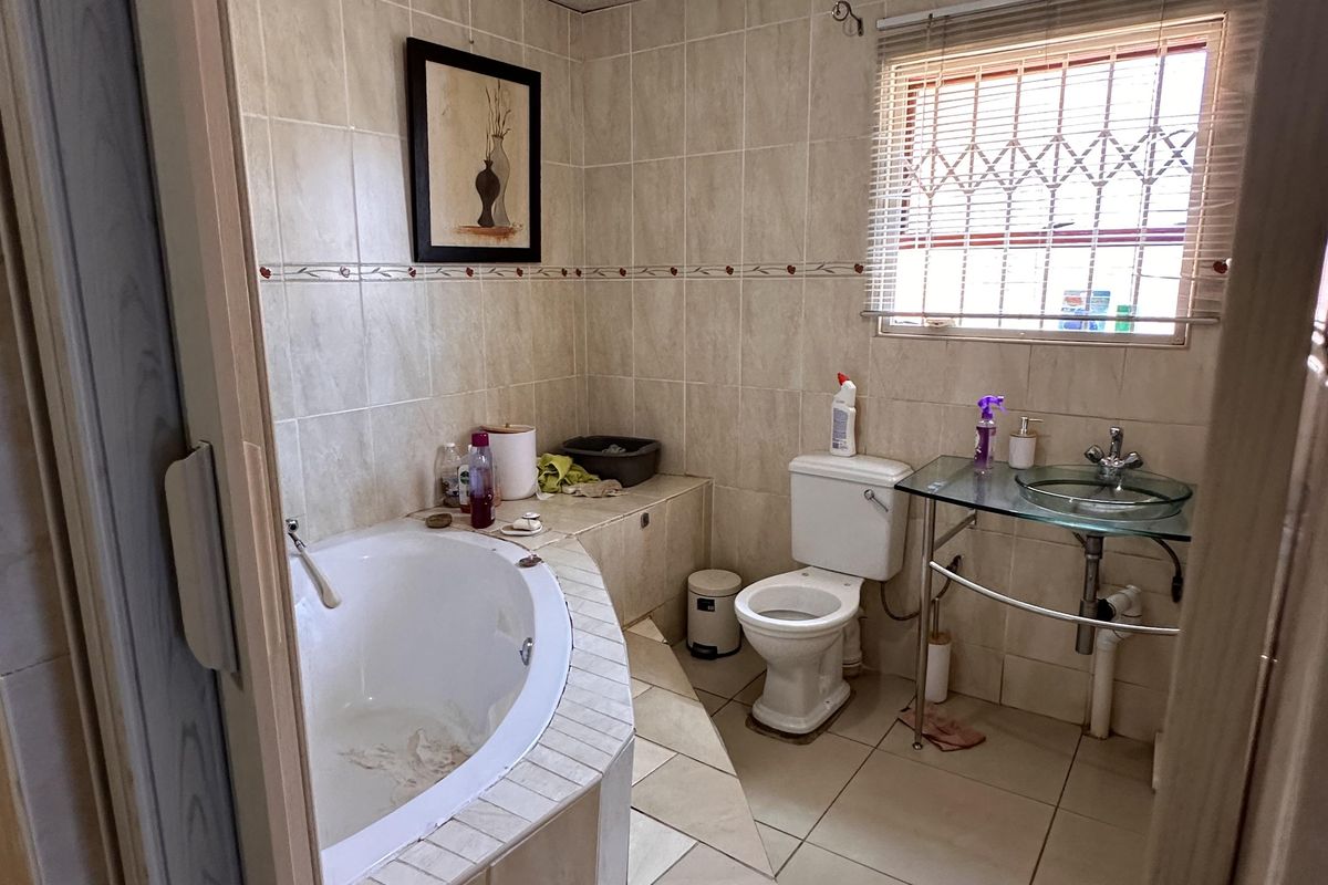 A functional bathroom featuring a corner bathtub, a glass vessel sink, and a toilet, finished with neutral wall and floor tiling.