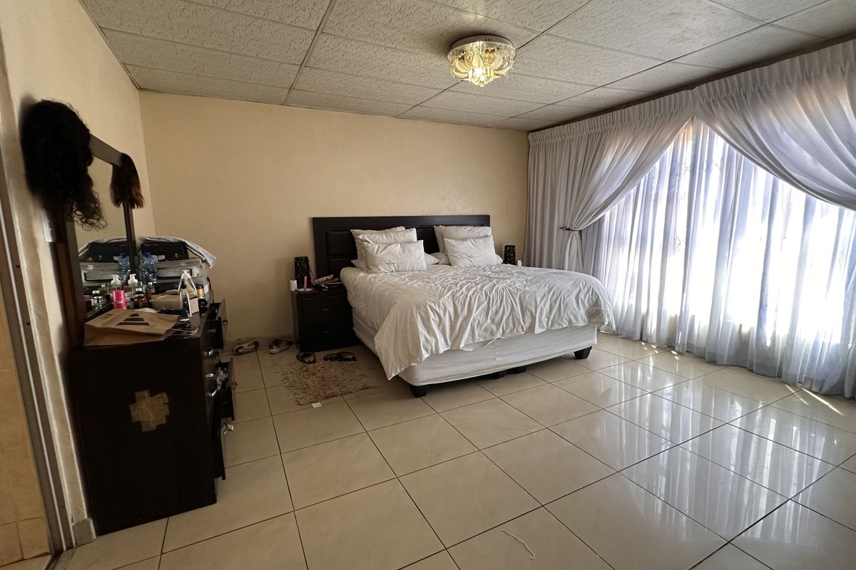 Spacious bedroom featuring large format floor tiles, a drop ceiling, and floor-to-ceiling curtains providing ample natural light.