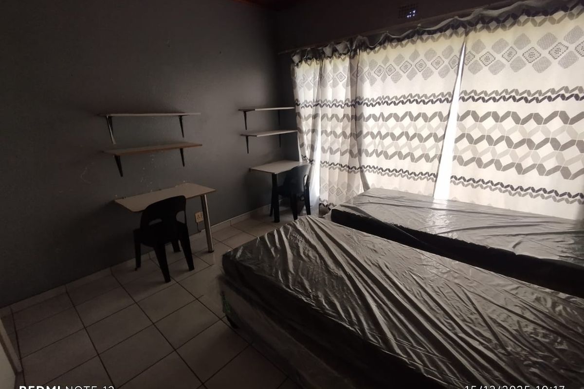 A functional bedroom featuring tiled flooring, built-in wall shelving, and large windows with curtains, suitable for a study or sleeping area.