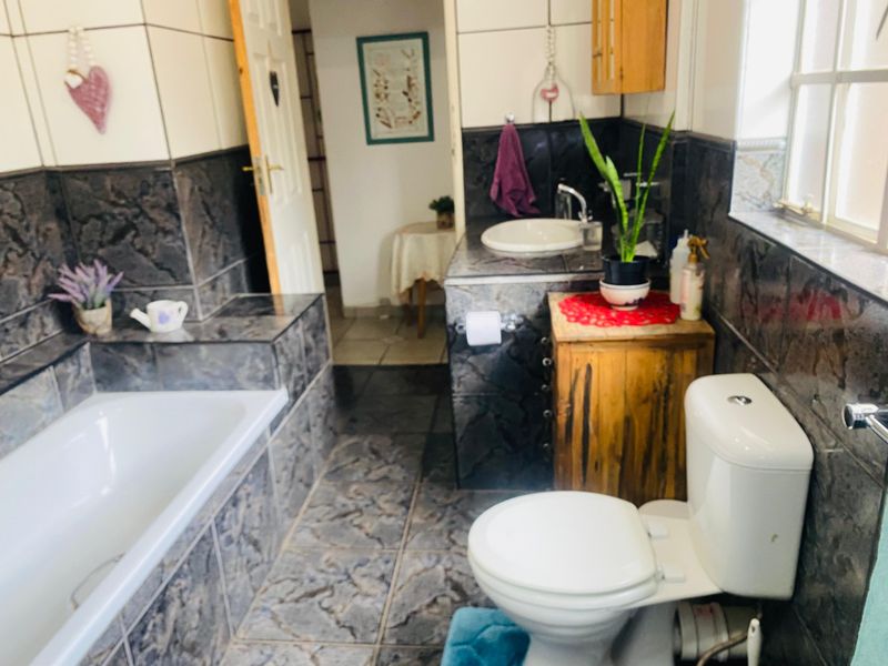 A functional bathroom featuring a built-in bathtub, vanity basin, and toilet with dark patterned wall and floor tiling.