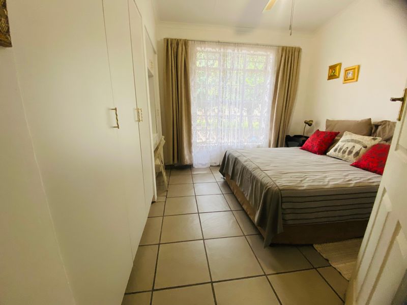 A bedroom featuring tiled flooring, built-in cupboards, and a ceiling fan, with natural light entering through a large window.