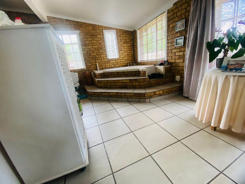 A spacious bathroom featuring a sunken bathtub with tiled steps, exposed brick walls, and large ceramic floor tiles.