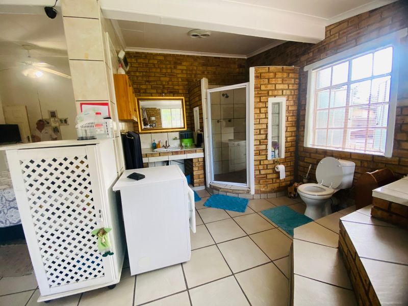 A functional bathroom featuring exposed brick walls, tiled flooring, a built-in vanity, and a separate shower enclosure.
