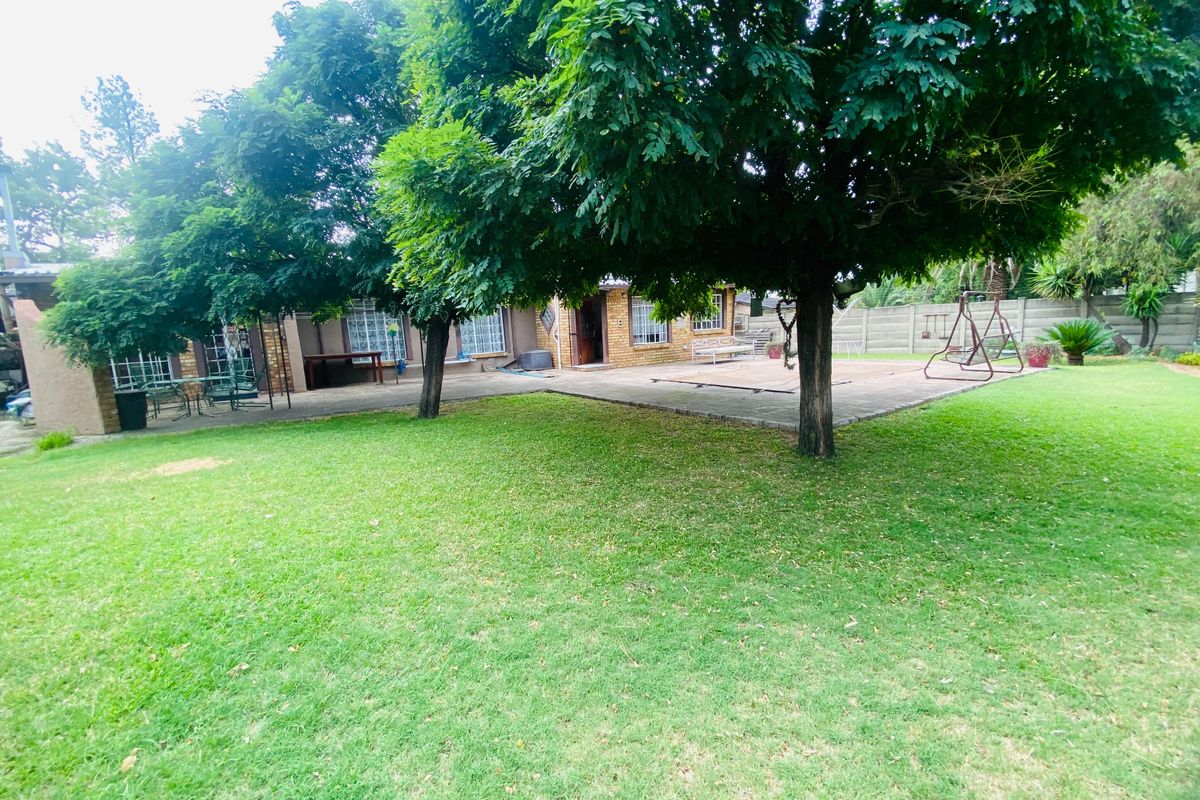 Spacious rear garden featuring a large lawn, mature trees, and a paved patio area adjacent to the brick-built house.