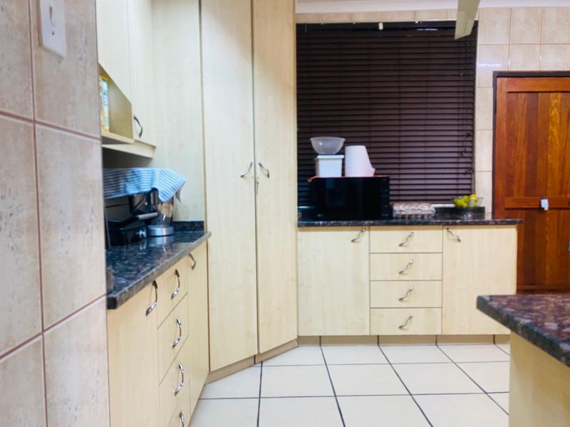 A functional kitchen featuring light-toned laminate cabinetry, dark granite countertops, tiled flooring, and a wooden door, providing a practical workspace.