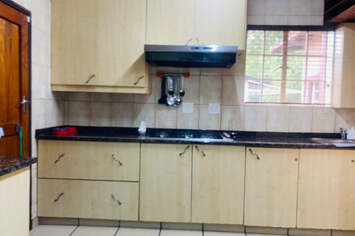 A functional kitchen featuring light wood-finish cabinetry, dark granite countertops, a built-in hob with extractor fan, and tiled splashbacks.
