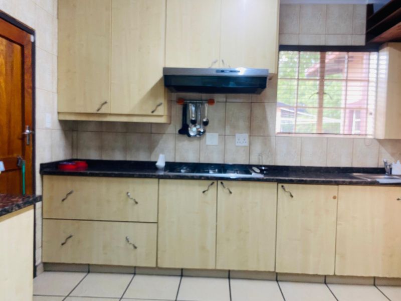 A functional kitchen featuring light wood-finish cabinetry, dark granite countertops, a built-in hob with extractor fan, and tiled splashbacks.