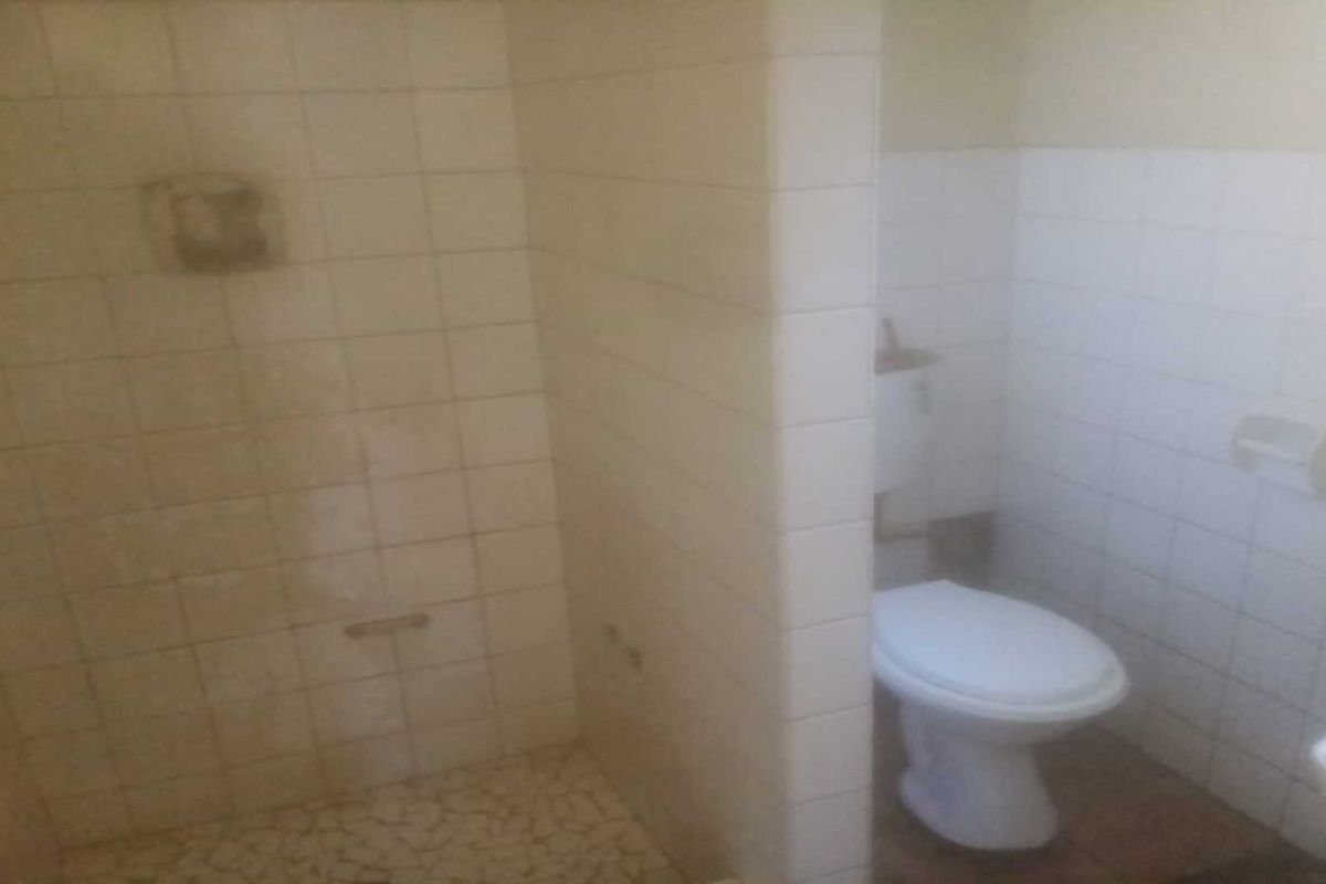 A functional bathroom featuring a tiled shower enclosure, a standard toilet, and wall-mounted fixtures, requiring cosmetic updates to modernize the space.
