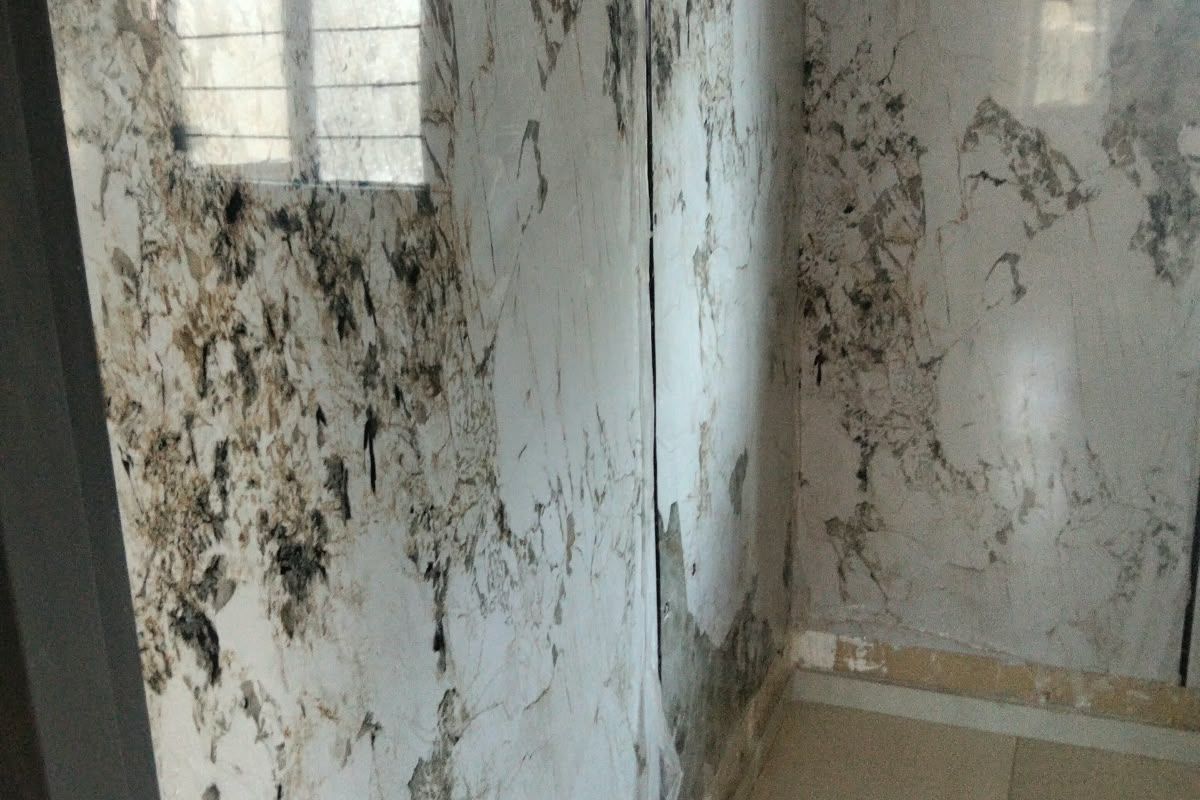 A bathroom space currently under renovation, featuring marble-effect wall panels and tiled flooring with an exposed plumbing outlet.