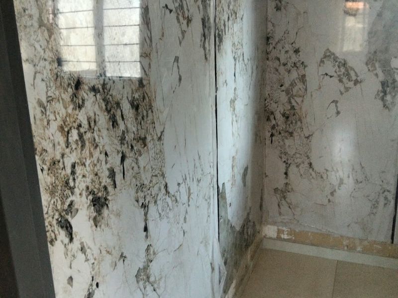 A bathroom space currently under renovation, featuring marble-effect wall panels and tiled flooring with an exposed plumbing outlet.