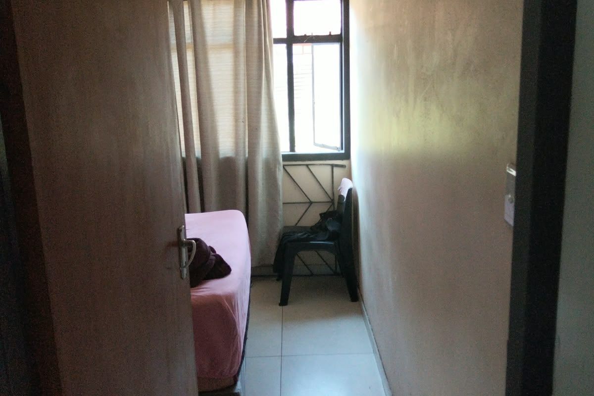 A compact bedroom featuring tiled flooring and a window with security bars, requiring cosmetic updates to improve its overall appeal.