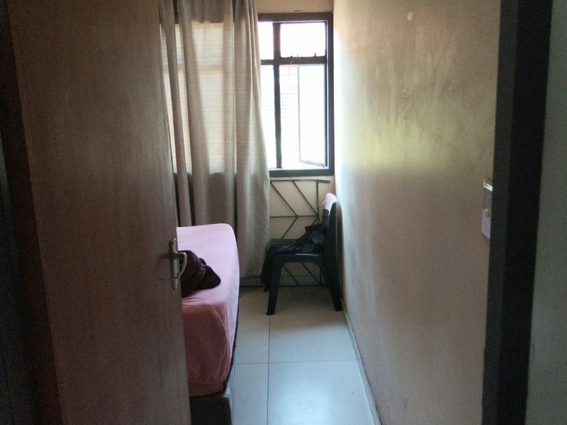 A compact bedroom featuring tiled flooring and a window with security bars, requiring cosmetic updates to improve its overall appeal.