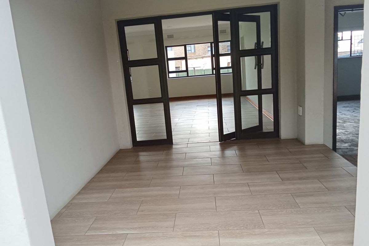 An open-plan living area featuring wood-look tiled flooring and dark-framed glass double doors leading to an adjacent room.