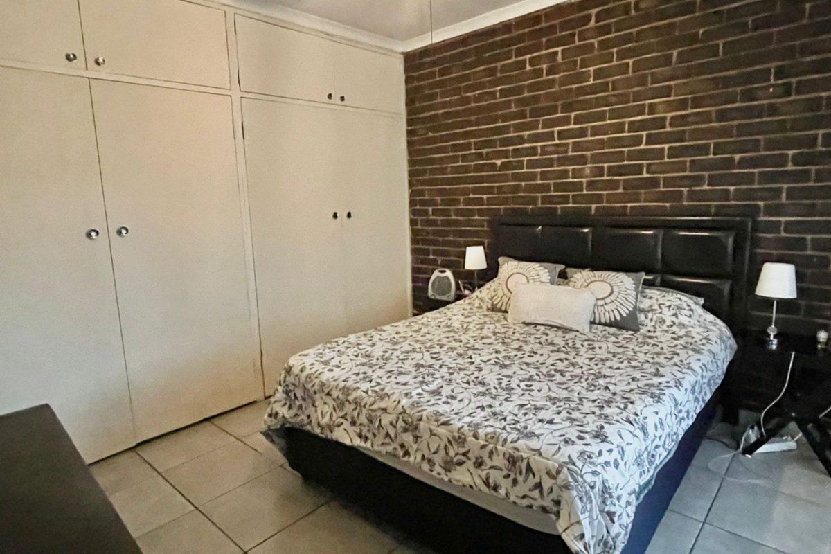 Bedroom featuring a prominent exposed brick feature wall and extensive built-in floor-to-ceiling cabinetry with tiled flooring.