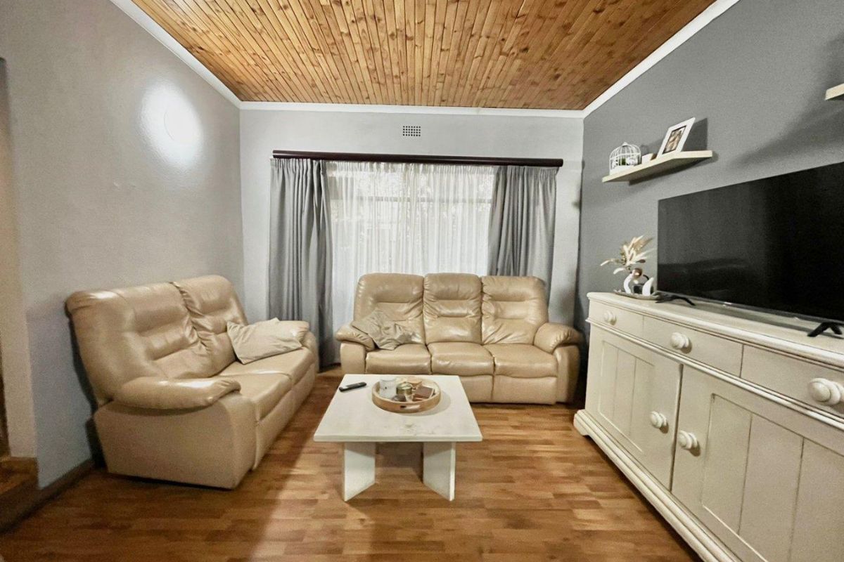 A cozy living room featuring warm timber-clad ceilings, laminate wood flooring, and a large window with curtain treatments.