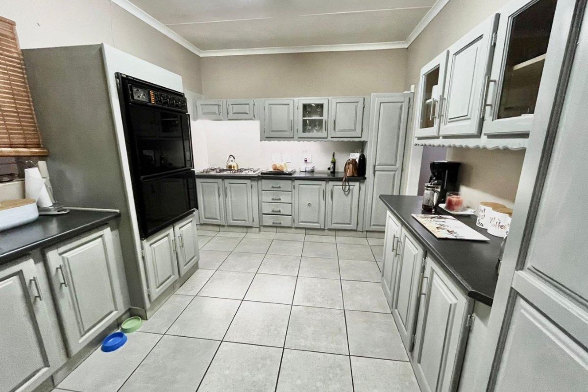 A functional kitchen featuring light grey cabinetry, dark countertops, tiled flooring, and a built-in double oven with a gas hob.