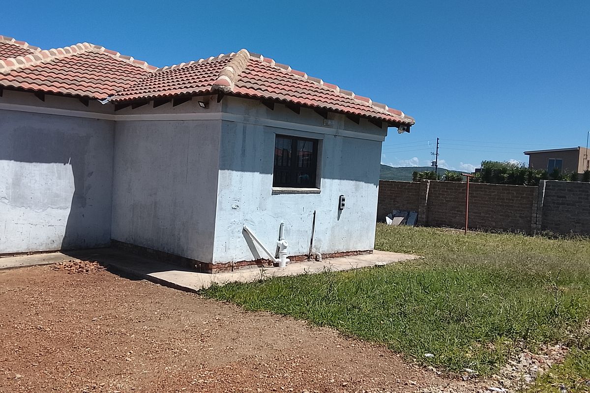 Rear view of the property showing the exterior wall, tiled roof, and surrounding yard area with basic landscaping.
