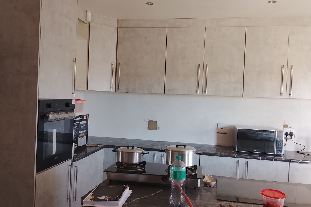 Modern kitchen featuring grey textured cabinetry, dark stone-look countertops, built-in oven, and a gas hob setup.