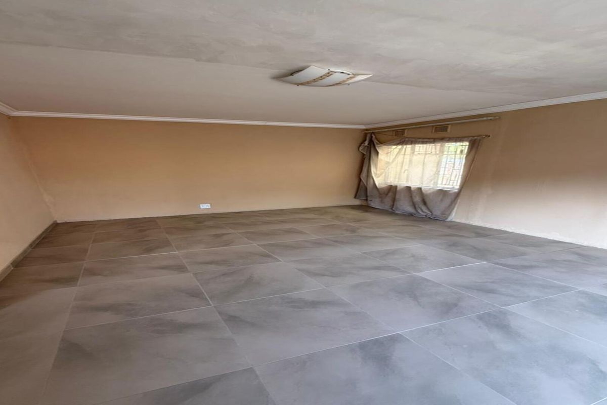 A spacious, empty living room featuring large format grey floor tiles, neutral wall tones, and a central ceiling light fixture.