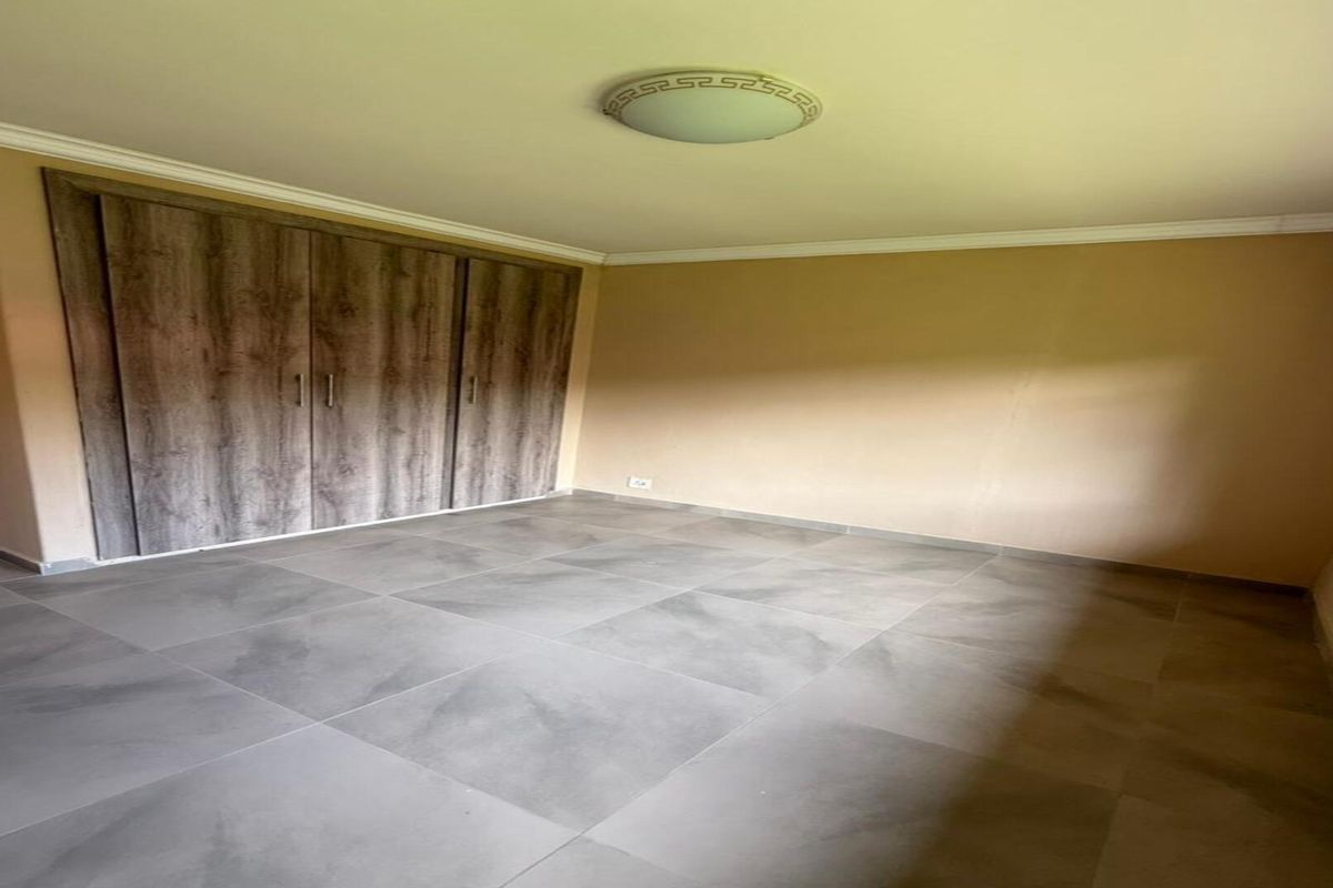 A bright, empty bedroom featuring large-format grey floor tiles and built-in wooden cabinetry with a modern finish.