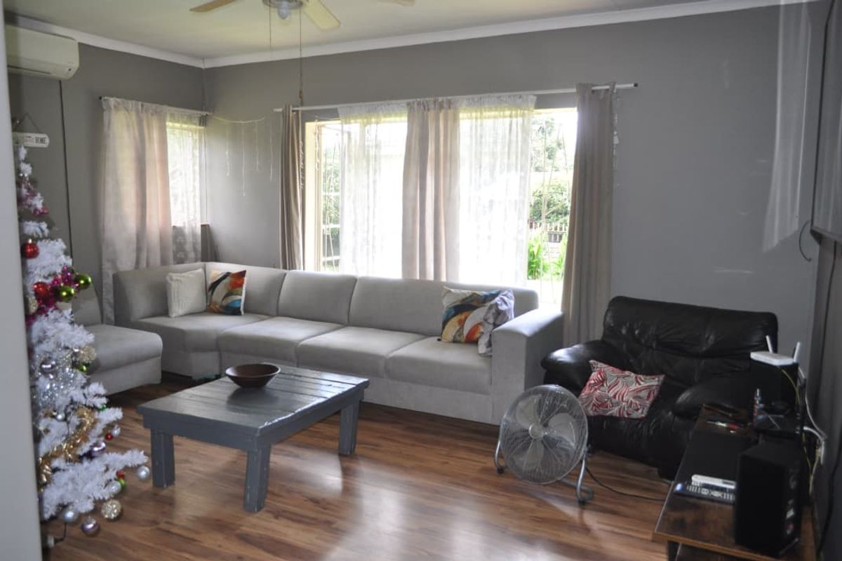 A comfortable living room featuring wood-look laminate flooring, large windows allowing natural light, and a ceiling fan for climate control.