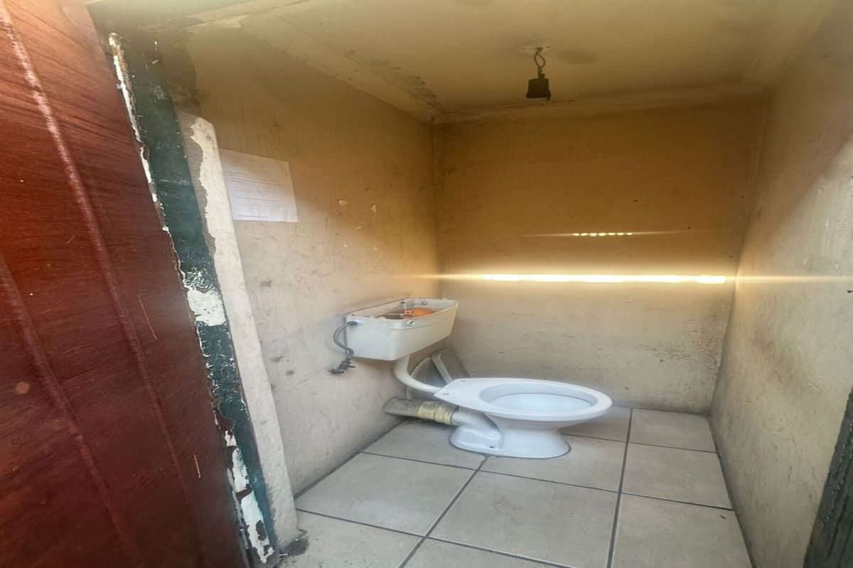 A small, dated bathroom featuring a standard toilet, tiled flooring, and walls in need of significant repair and refurbishment.