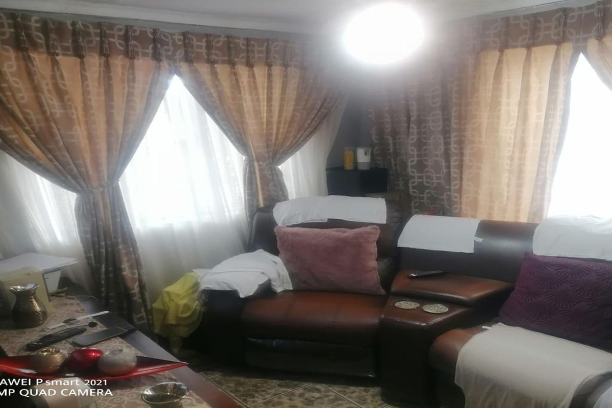 A living room featuring tiled flooring and large windows with curtains, providing natural light to the space.