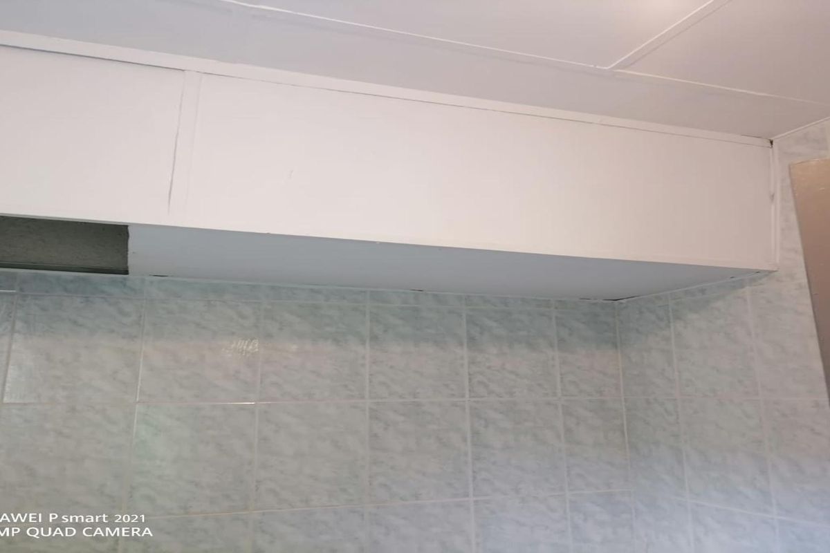 A close-up view of dated kitchen cabinetry and tiled wall finishes, showing signs of wear and requiring potential cosmetic updates.