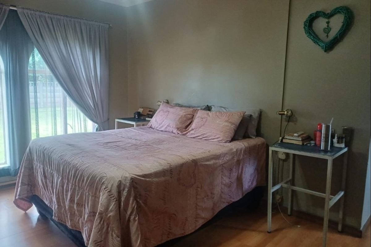 A bedroom featuring laminate flooring, large windows with curtains, and wall-mounted lighting fixtures.
