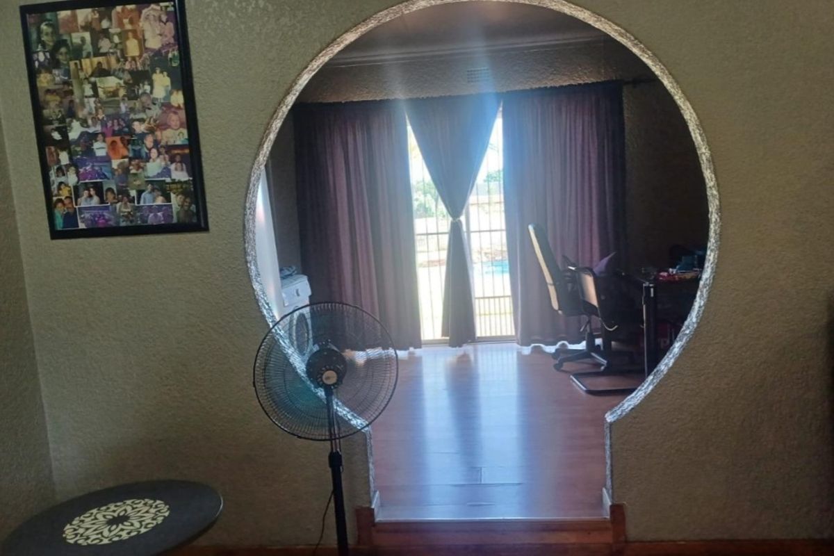 A living area featuring a distinctive circular archway leading to an adjacent room with laminate flooring and access to the exterior.