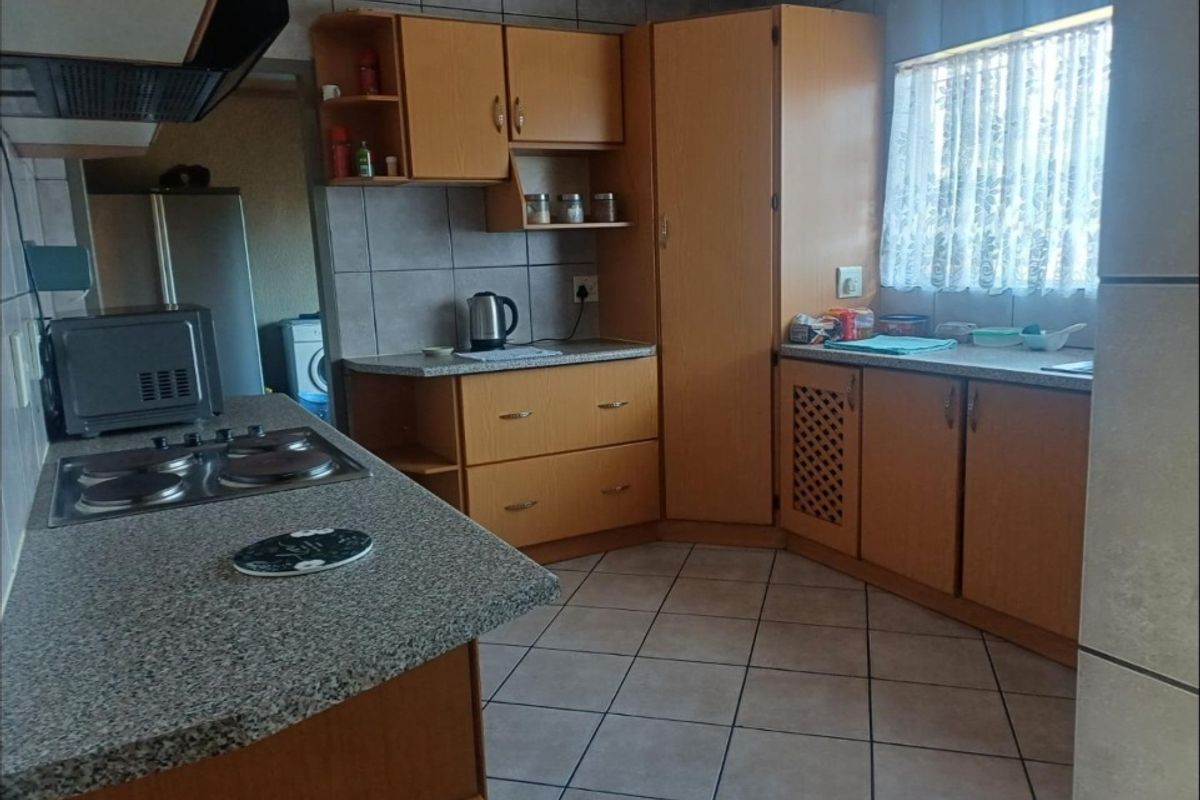 A functional kitchen featuring wooden cabinetry, granite-look countertops, a built-in hob, and tiled flooring with a window providing natural light.