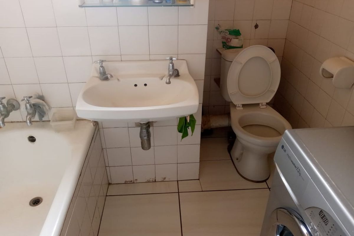 A dated bathroom featuring a standard bathtub, wall-mounted basin, and toilet, with tiled walls and flooring requiring maintenance or renovation.