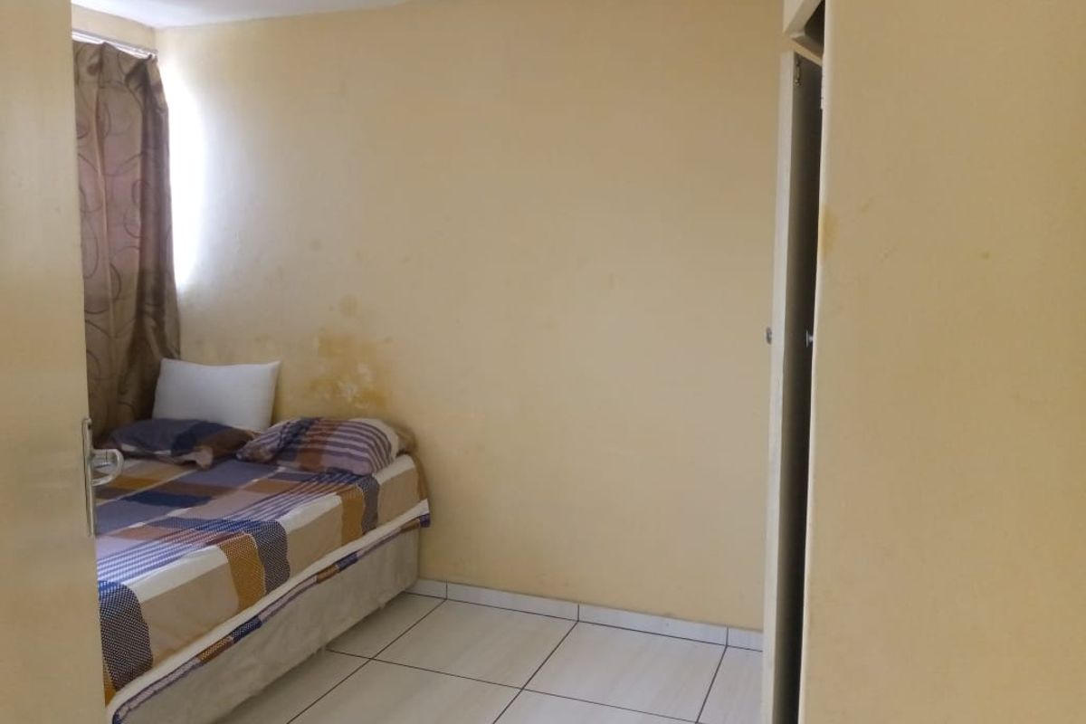 A bedroom featuring tiled flooring and built-in closet space, currently showing signs of wall moisture damage and requiring cosmetic refurbishment.