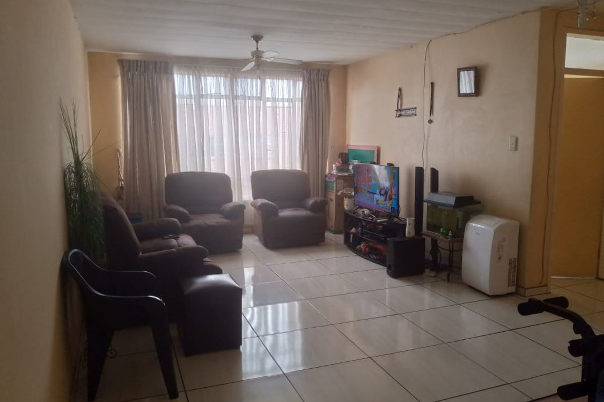 A living room featuring large format floor tiles, a ceiling fan, and a large window with curtains, providing a functional living space.