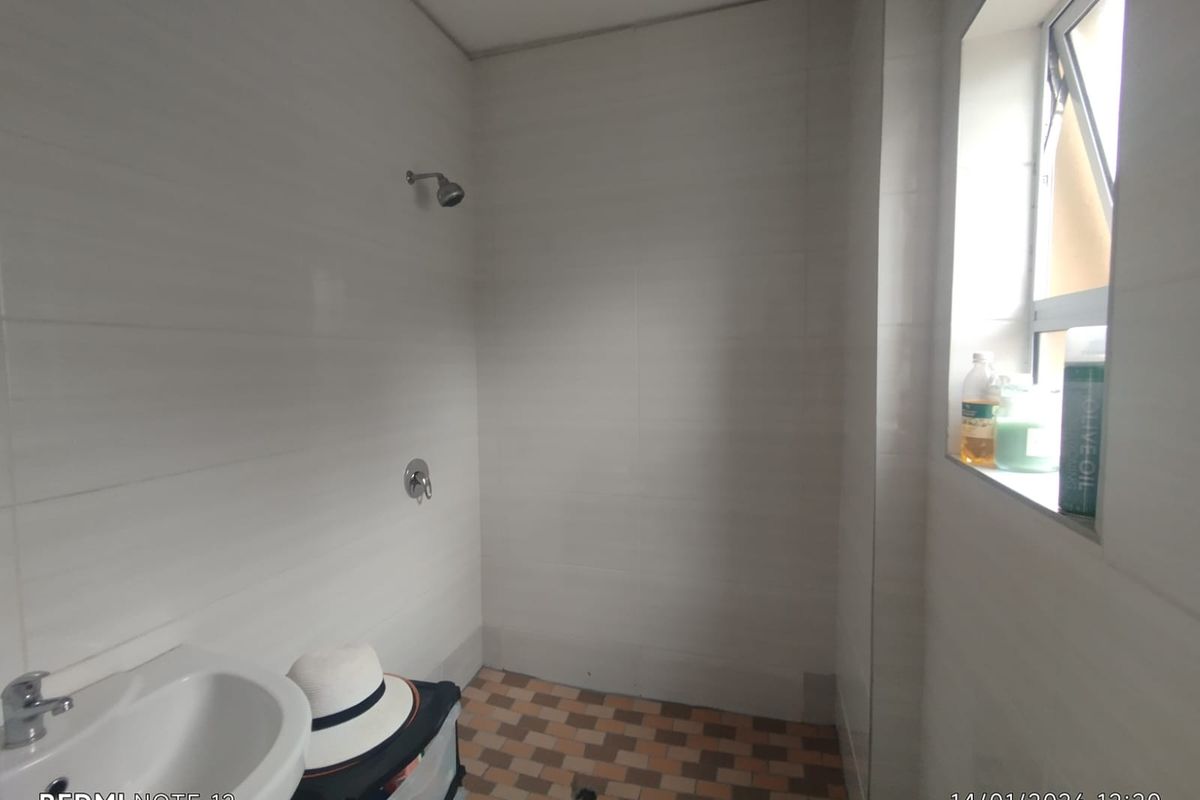 A functional bathroom featuring a wall-mounted shower head, basin, and tiled flooring with a side window for natural light.