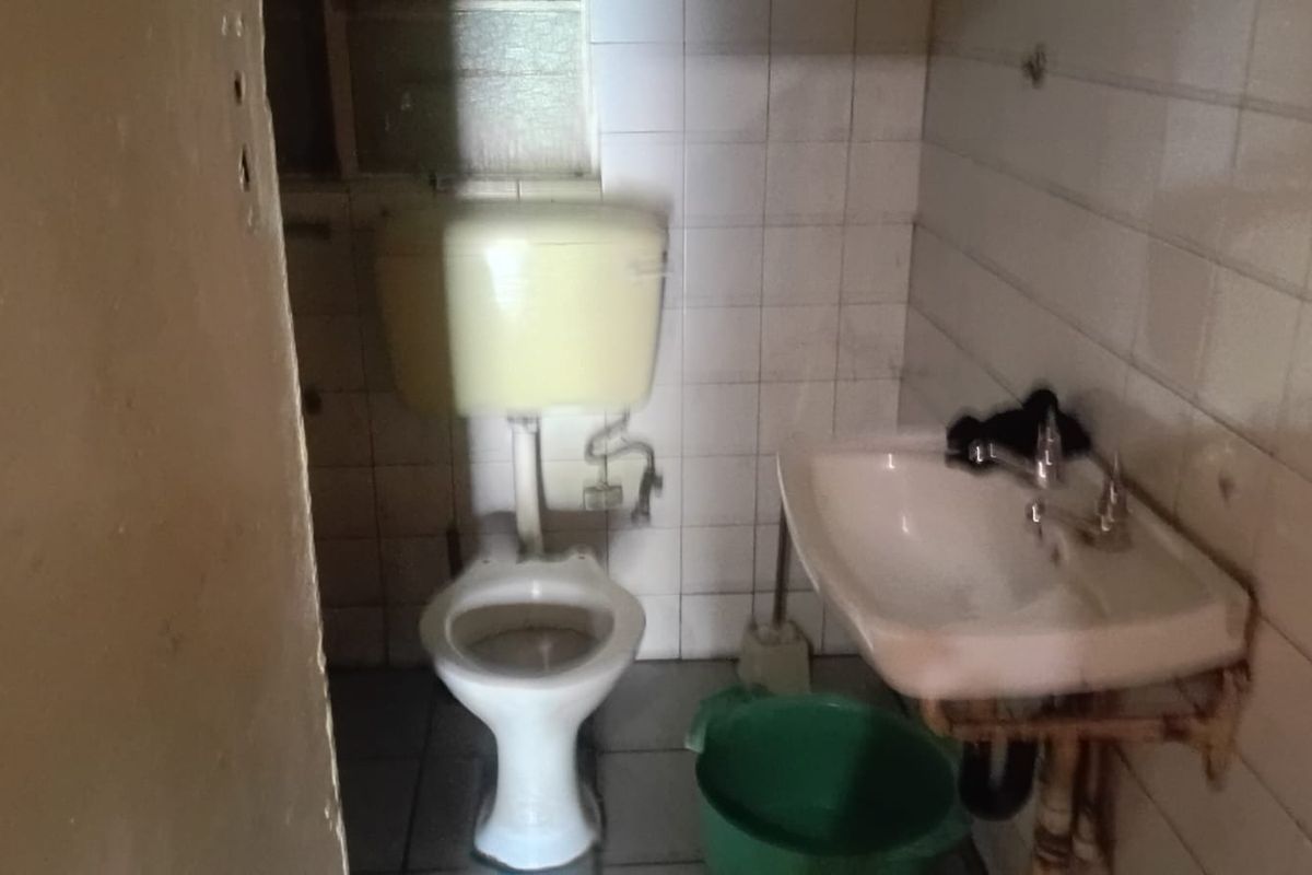 A dated bathroom featuring a wall-mounted toilet cistern and a basic pedestal sink with tiled walls and flooring.