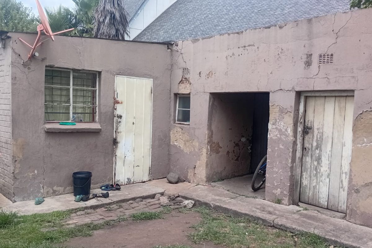 Rear exterior view of the property showing weathered masonry walls, multiple access doors, and a small paved area requiring significant maintenance and repair.